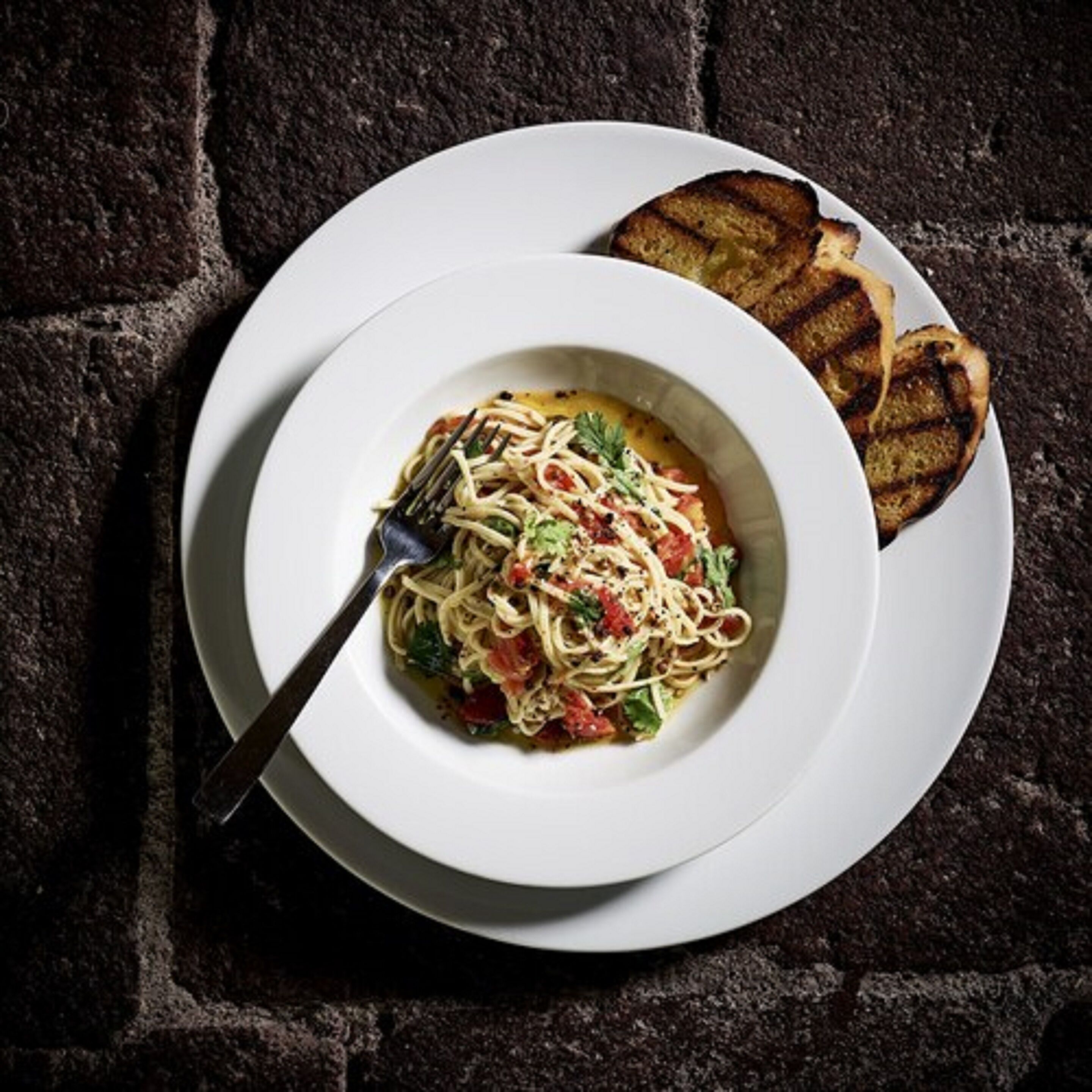 A plate of spaghetti with a fork on a white plate, placed on a dark textured surface.