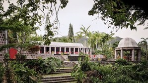 A building with a covered walkway, surrounded by lush greenery and a stone structure.