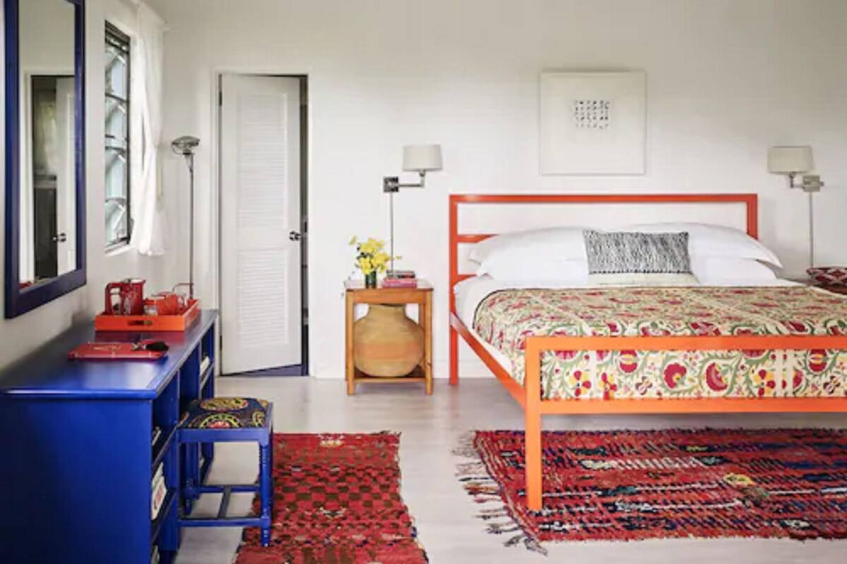 A bedroom with a wooden bed, a blue desk, a red chair, and a patterned rug.