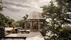 A gazebo with a dome roof, surrounded by a water feature and lush greenery.