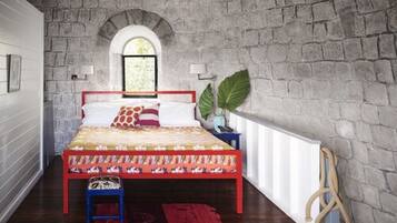A bedroom with a stone wall, a bed with a colorful headboard, a window, and a plant.