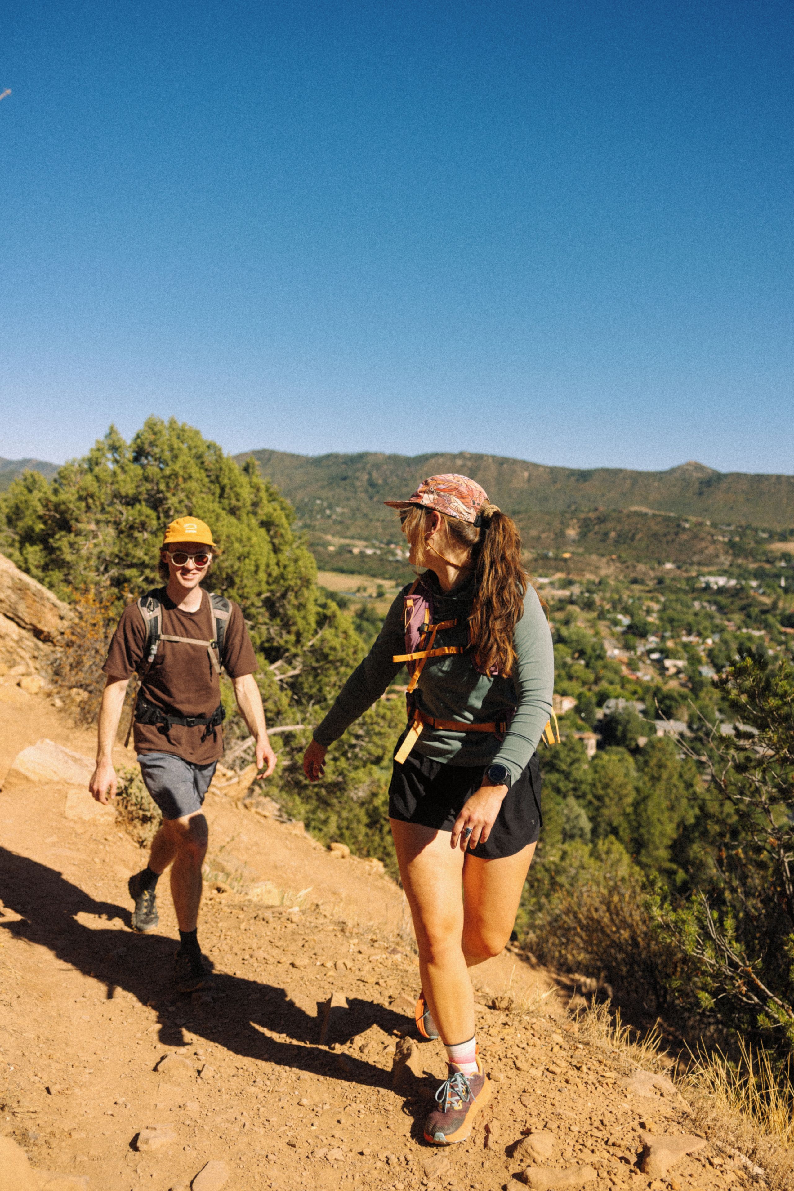 Two people hiking on a dirt path with a mountainous landscape in the background.