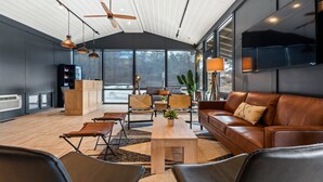 A modern living room with a large window, a ceiling fan, and a flat-screen TV mounted on the wall.