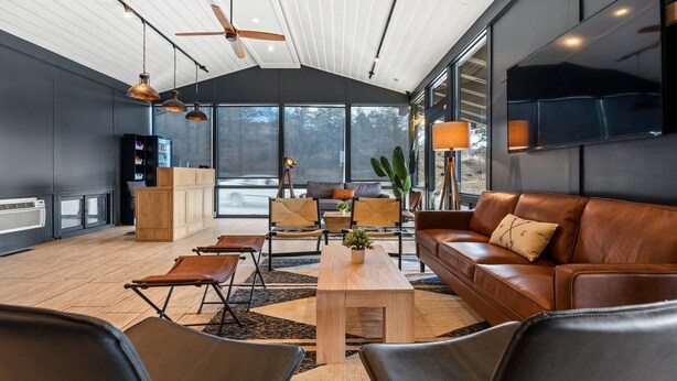A modern living room with a large window, a ceiling fan, and a flat-screen TV mounted on the wall.