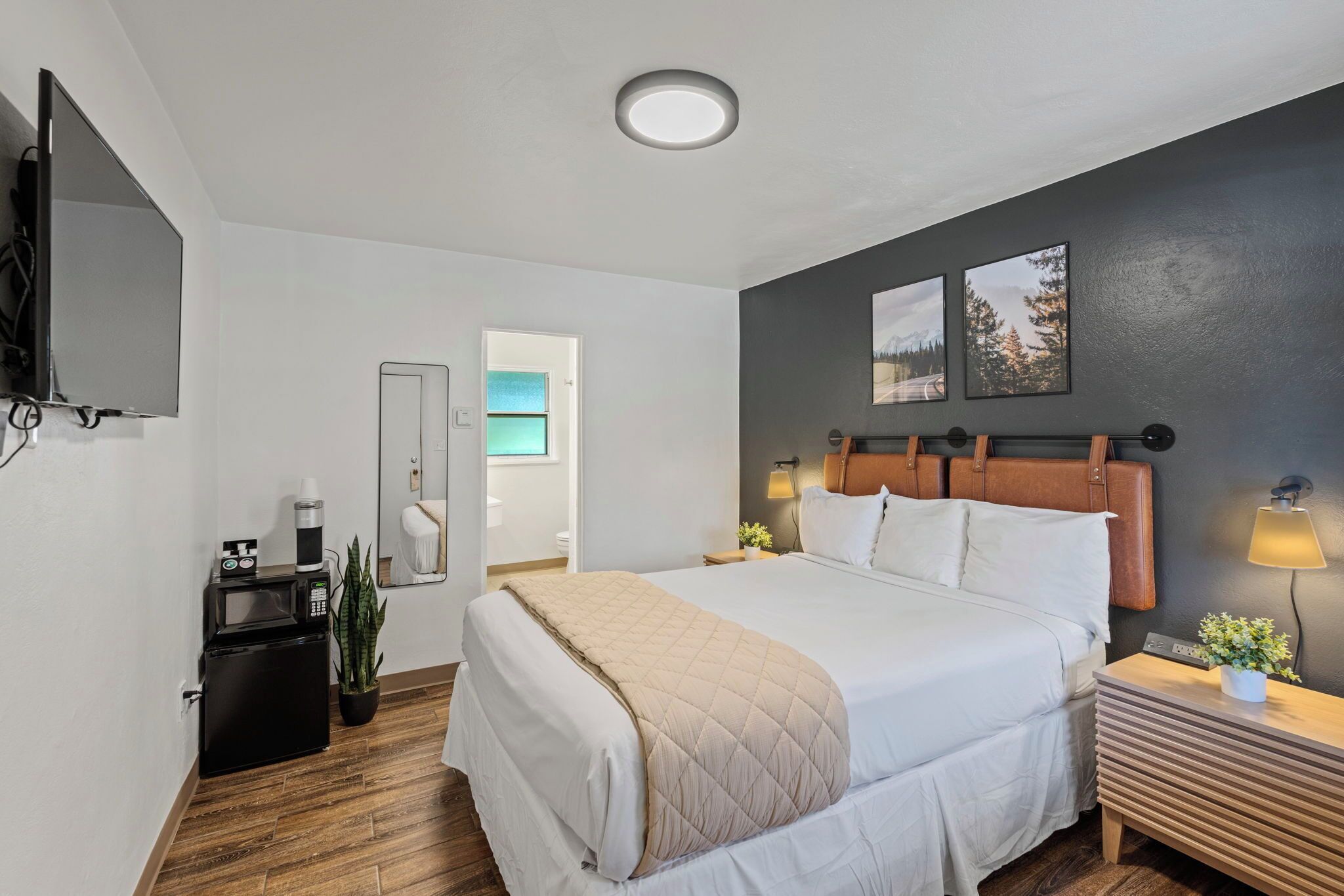 A hotel room with a large bed, bedside tables, a TV, a small fridge, and a mirror.