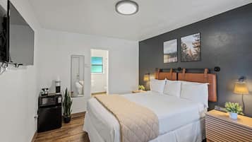 A hotel room with a large bed, bedside tables, a TV, a small fridge, and a mirror.
