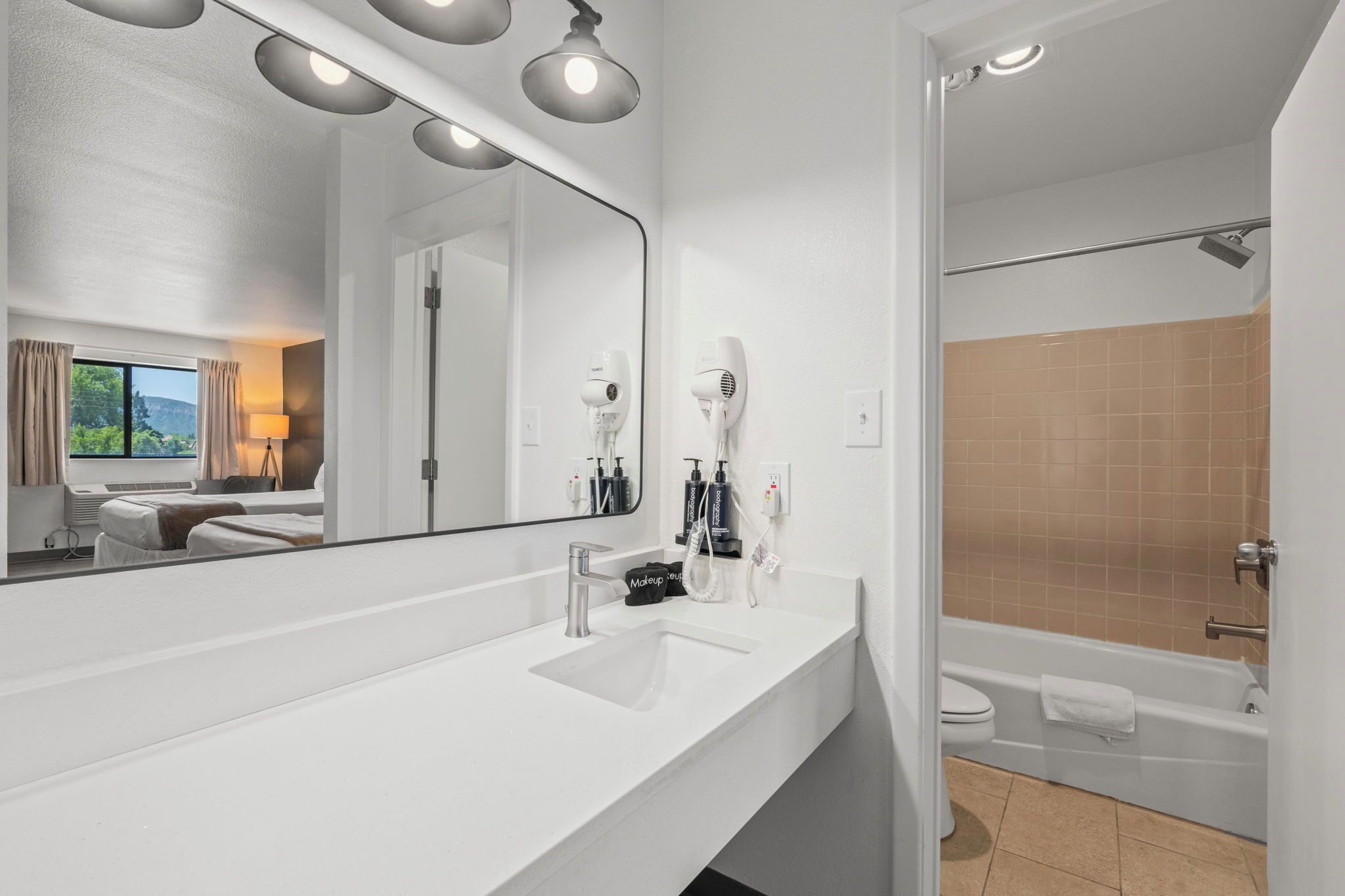 Ein modernes Badezimmer mit großem Spiegel, weißem Waschbecken und einer Badewanne.