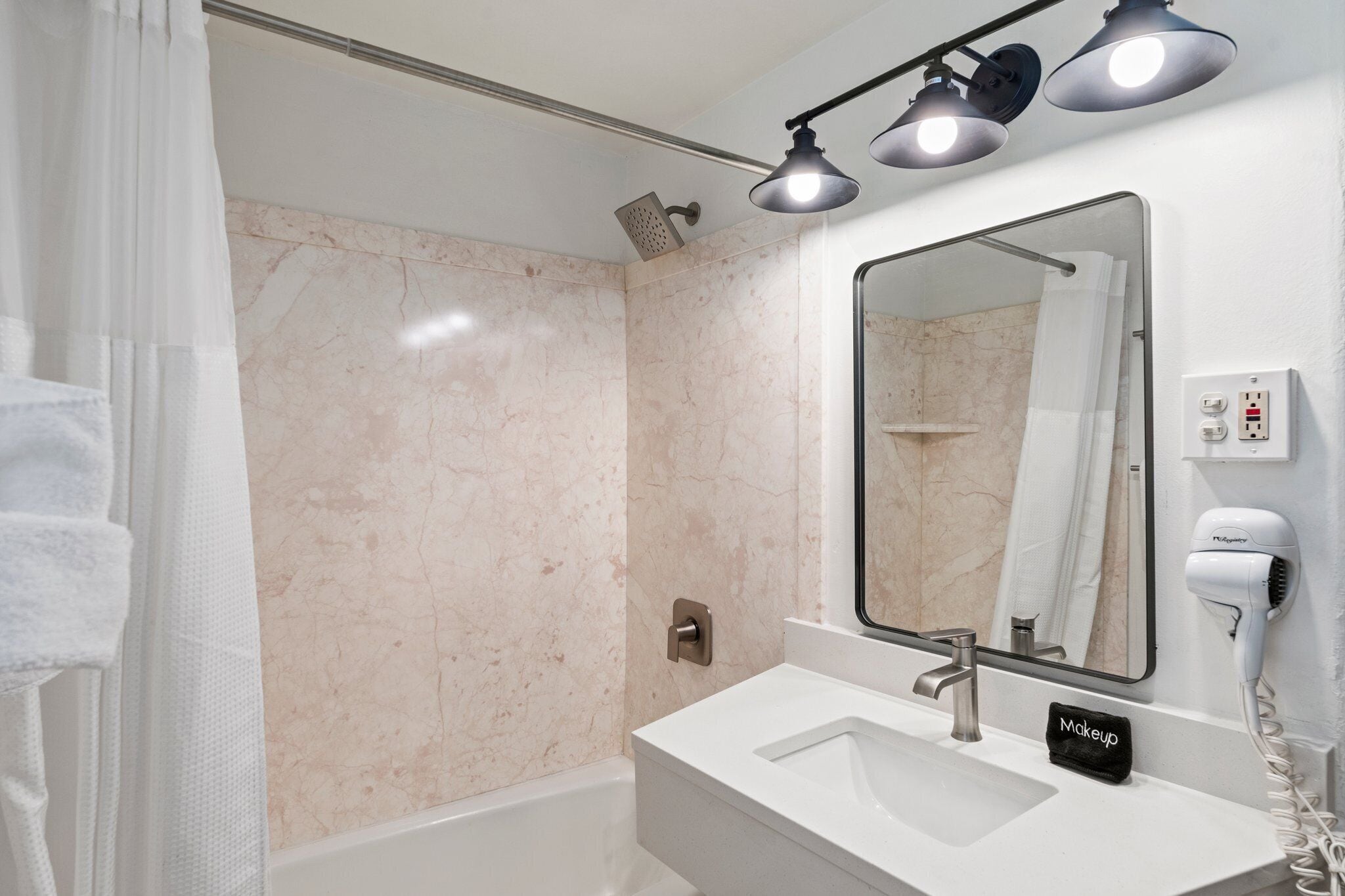 Un bagno moderno con una parete in marmo, un lavandino, uno specchio, un soffione della doccia e un asciugacapelli.