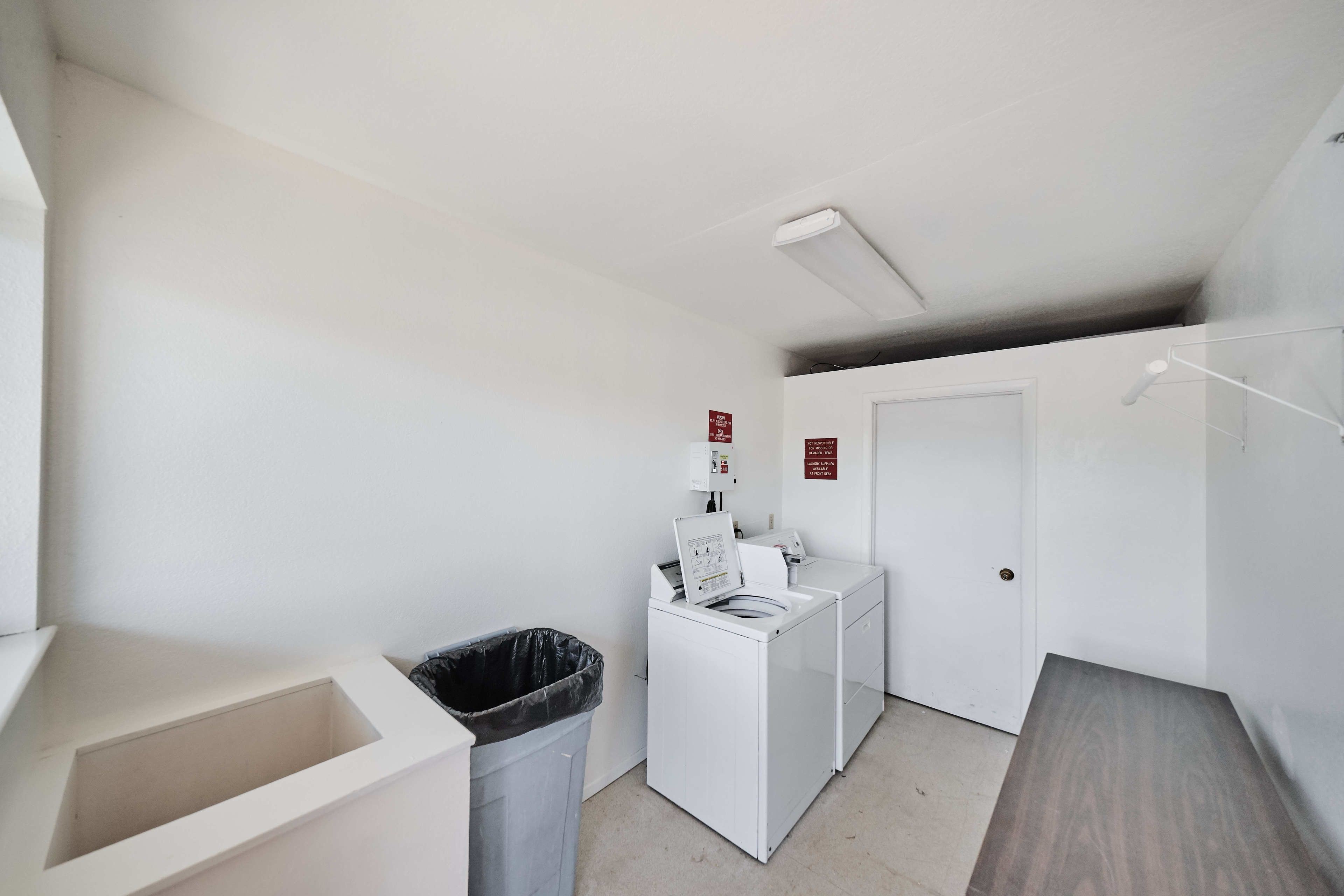 A laundry room with a washing machine, dryer, and trash bin.