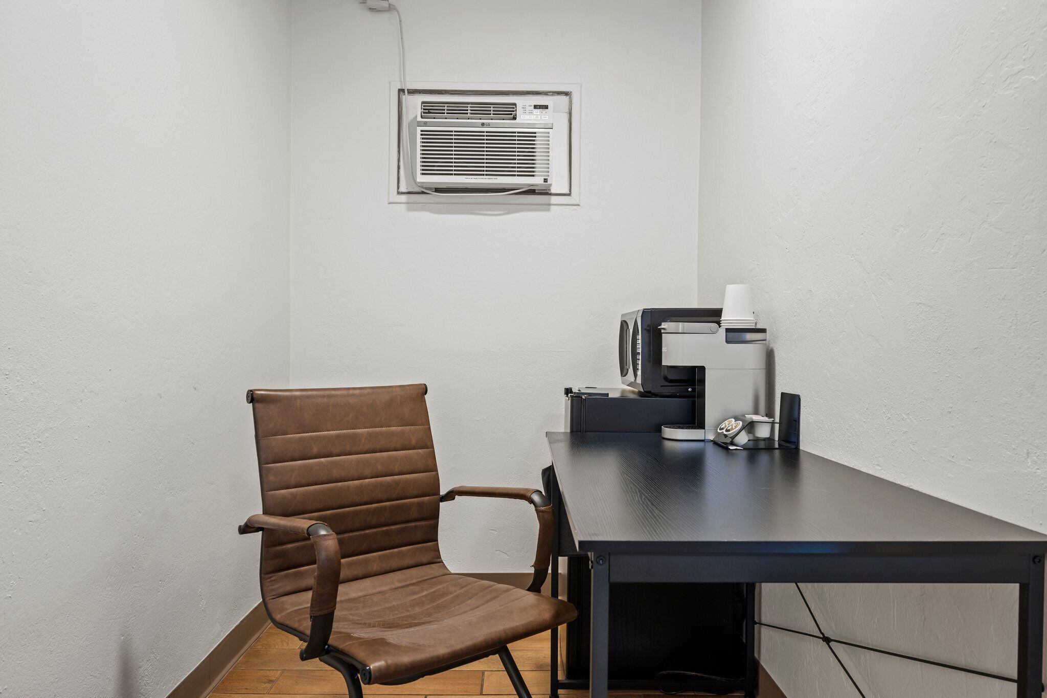 A conference room with a brown leather chair, a dark table, a white air conditioning unit, and a coffee machine.