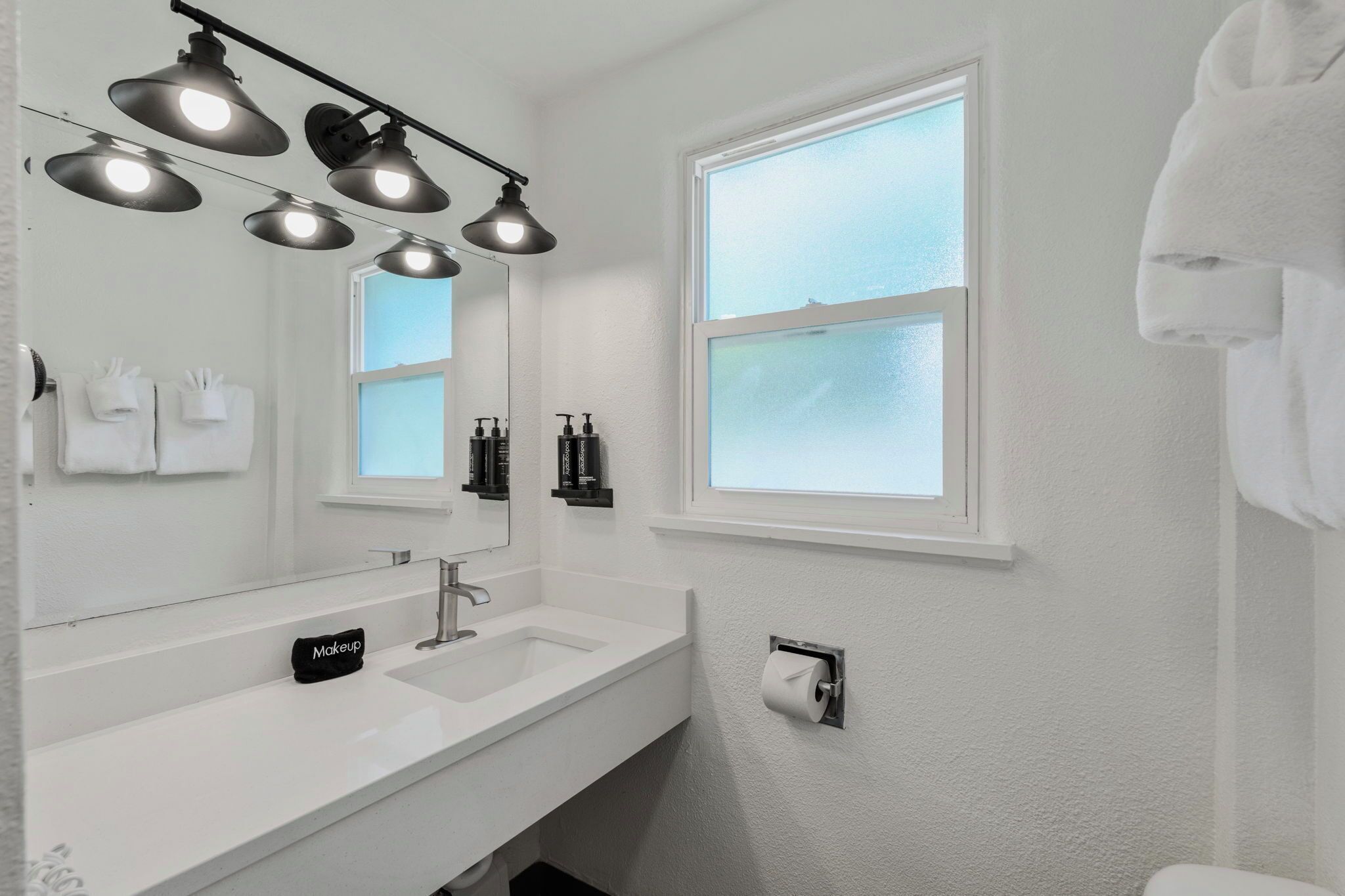 A modern bathroom with a white sink, a large mirror, and three pendant lights.