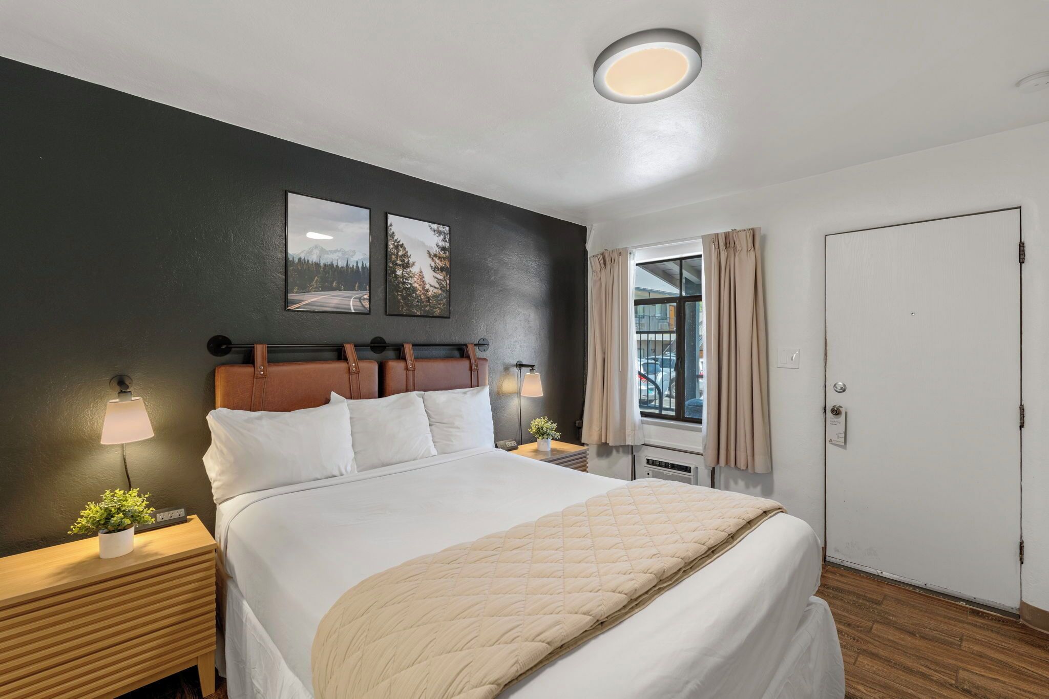 Un dormitorio con cama, lámparas de noche, mesita de noche, ventana con cortinas y puerta.
