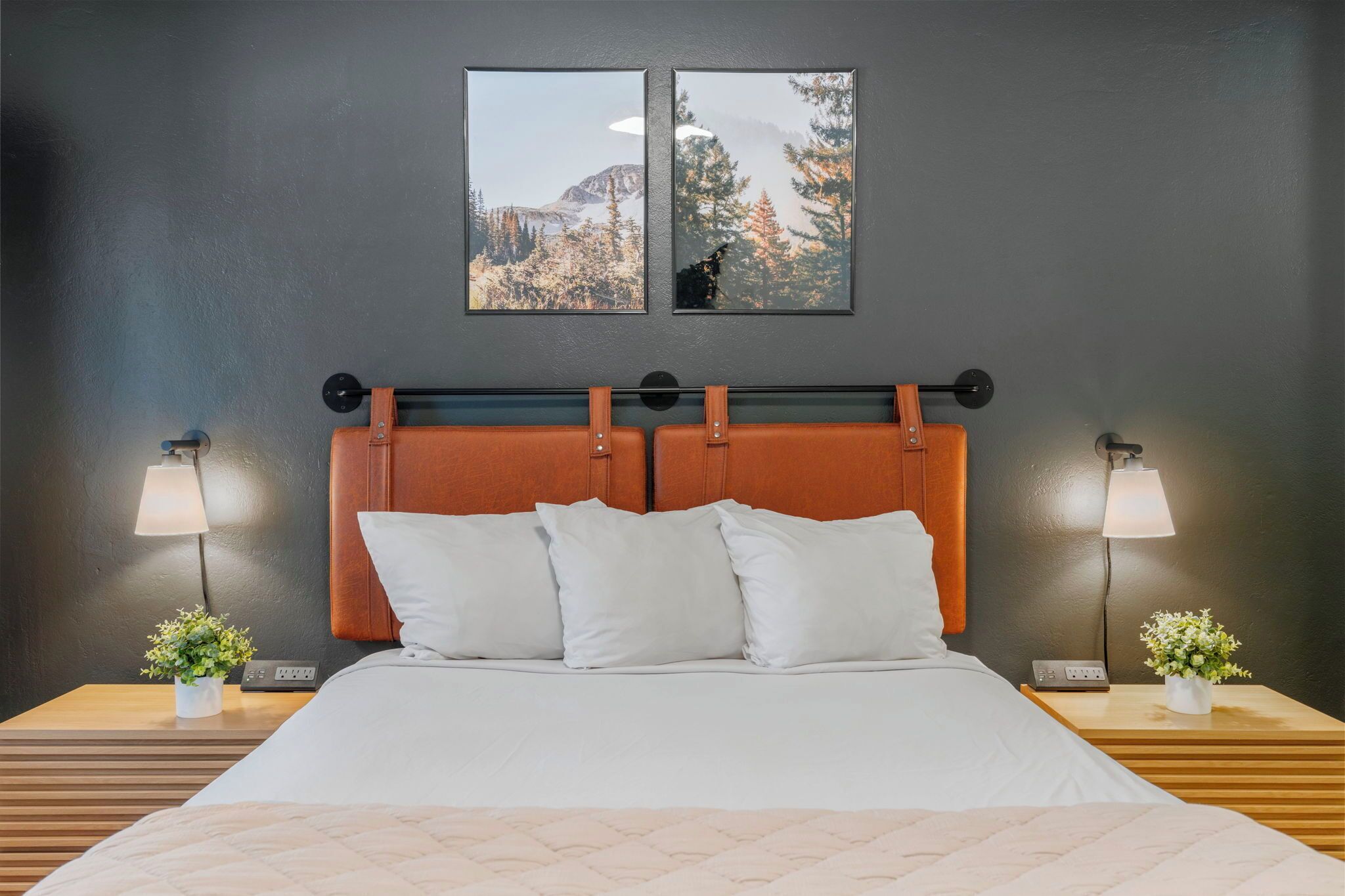 Hotelkamer met een bed, twee nachtkastjes, een hoofdbord, twee aan de muur bevestigde fotolijstjes en twee wandlampen.