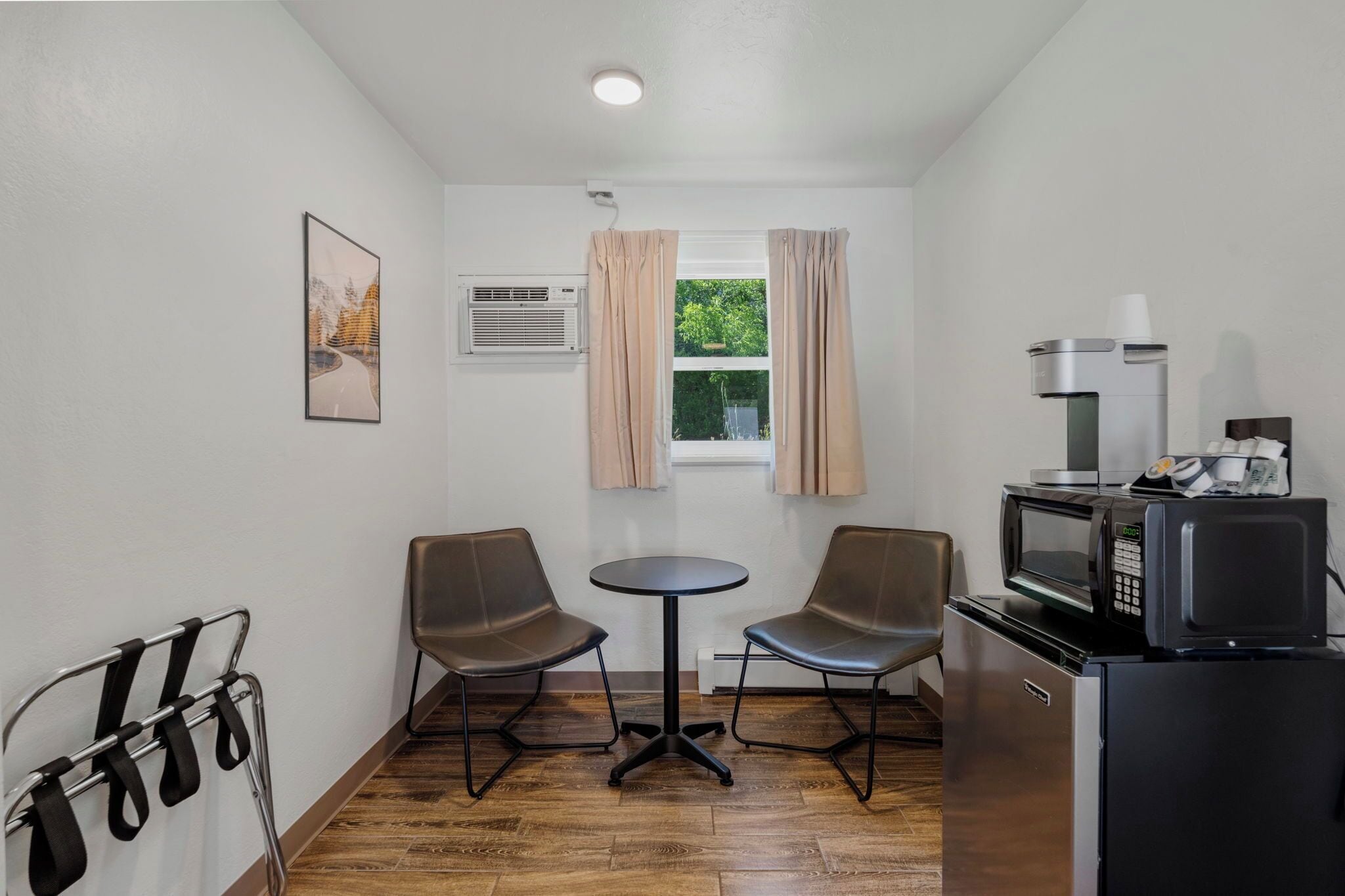 Una cocina compacta con comedor, microondas, refrigerador y ventana con cortinas.