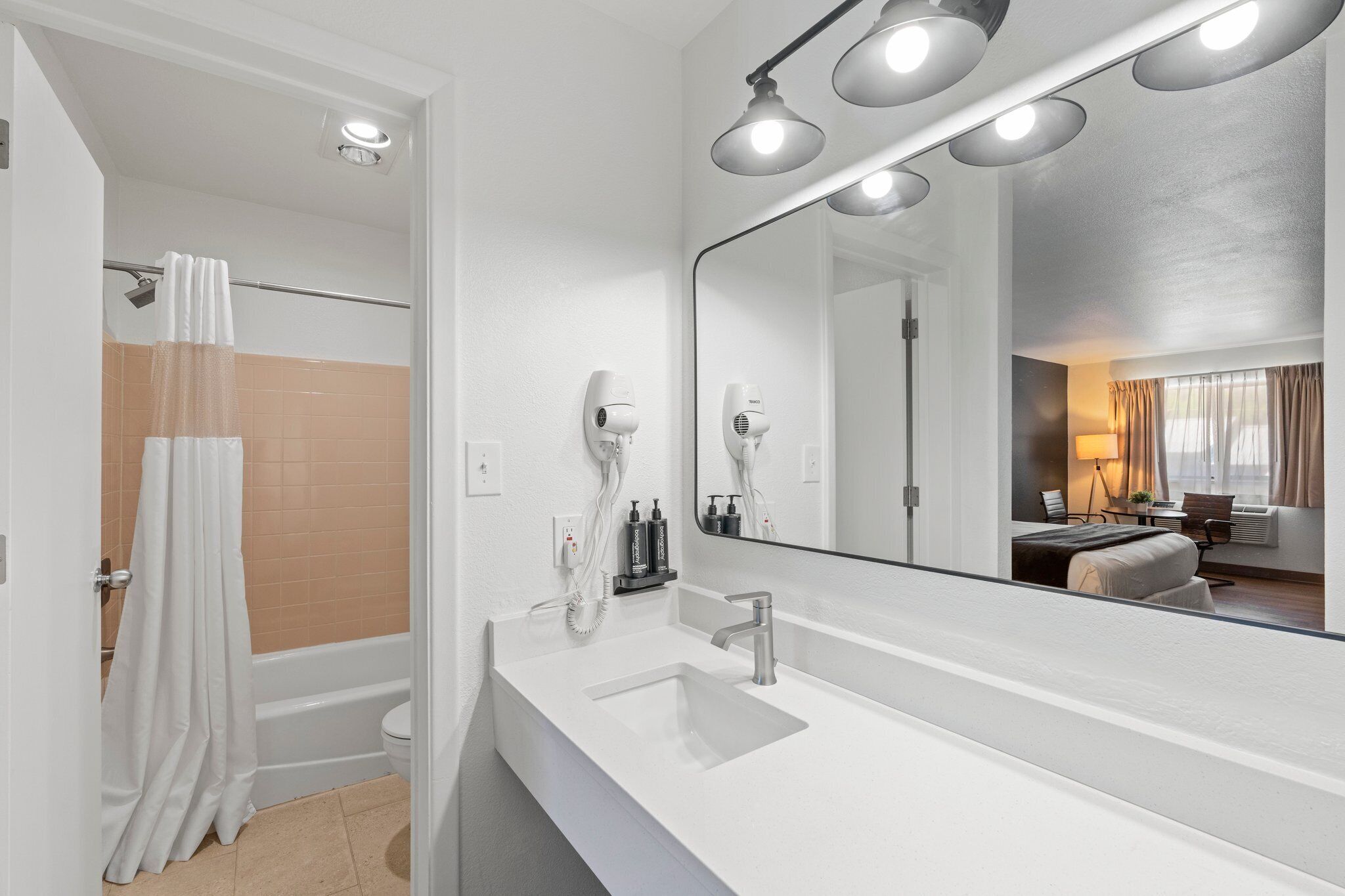 A modern bathroom with a large mirror, a white sink, and a shower area.