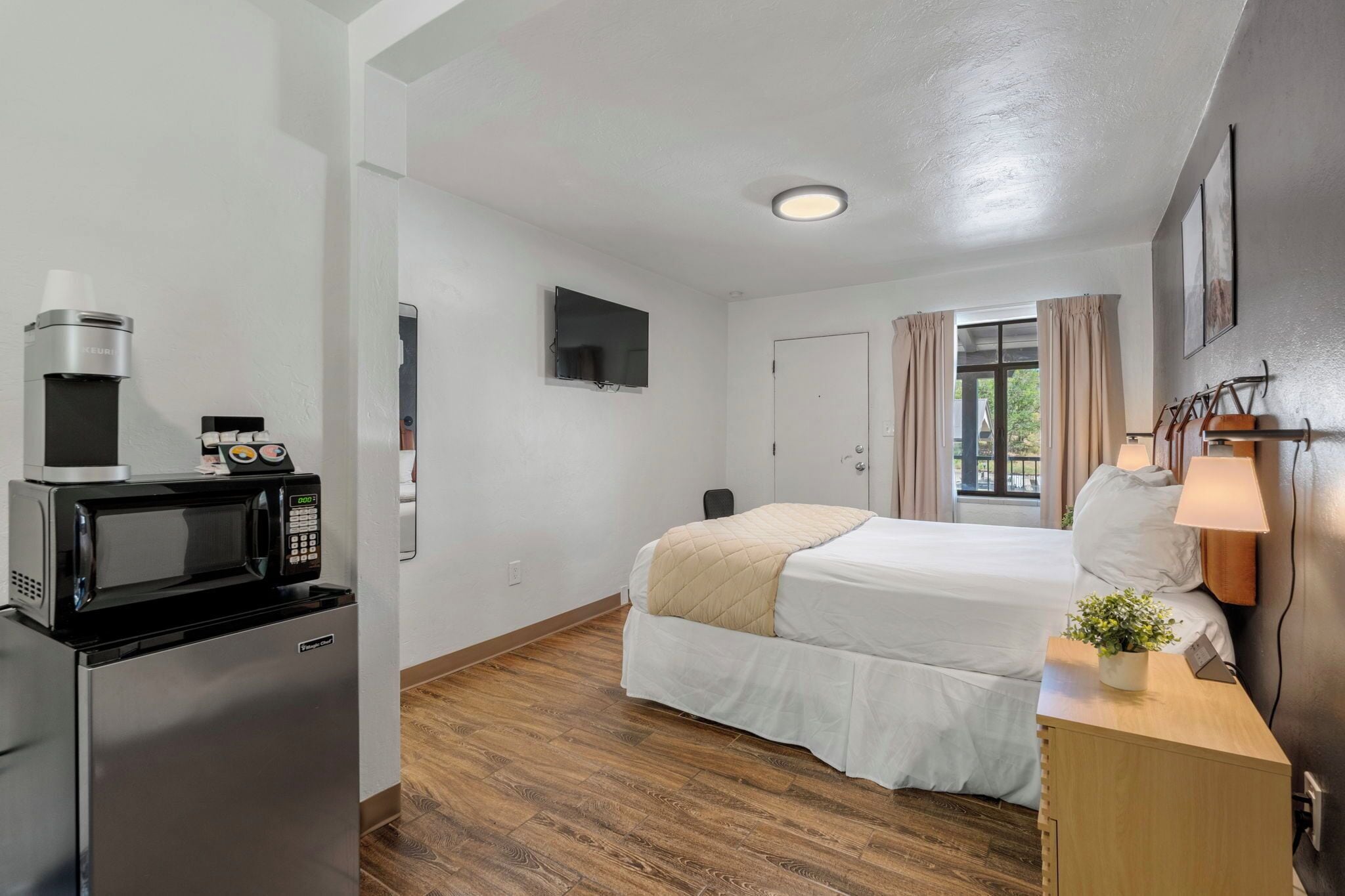 A hotel room with a bed, a desk with a lamp, a microwave, and a refrigerator.