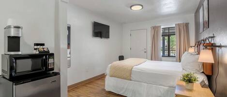 Ett hotellrum med en säng, ett skrivbord med en lampa, en mikrovågsugn och ett kylskåp.