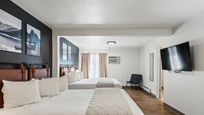 Hotellihuone, jossa on kaksi sänkyä, televisio, tuoli ja taideteoksia seinillä.