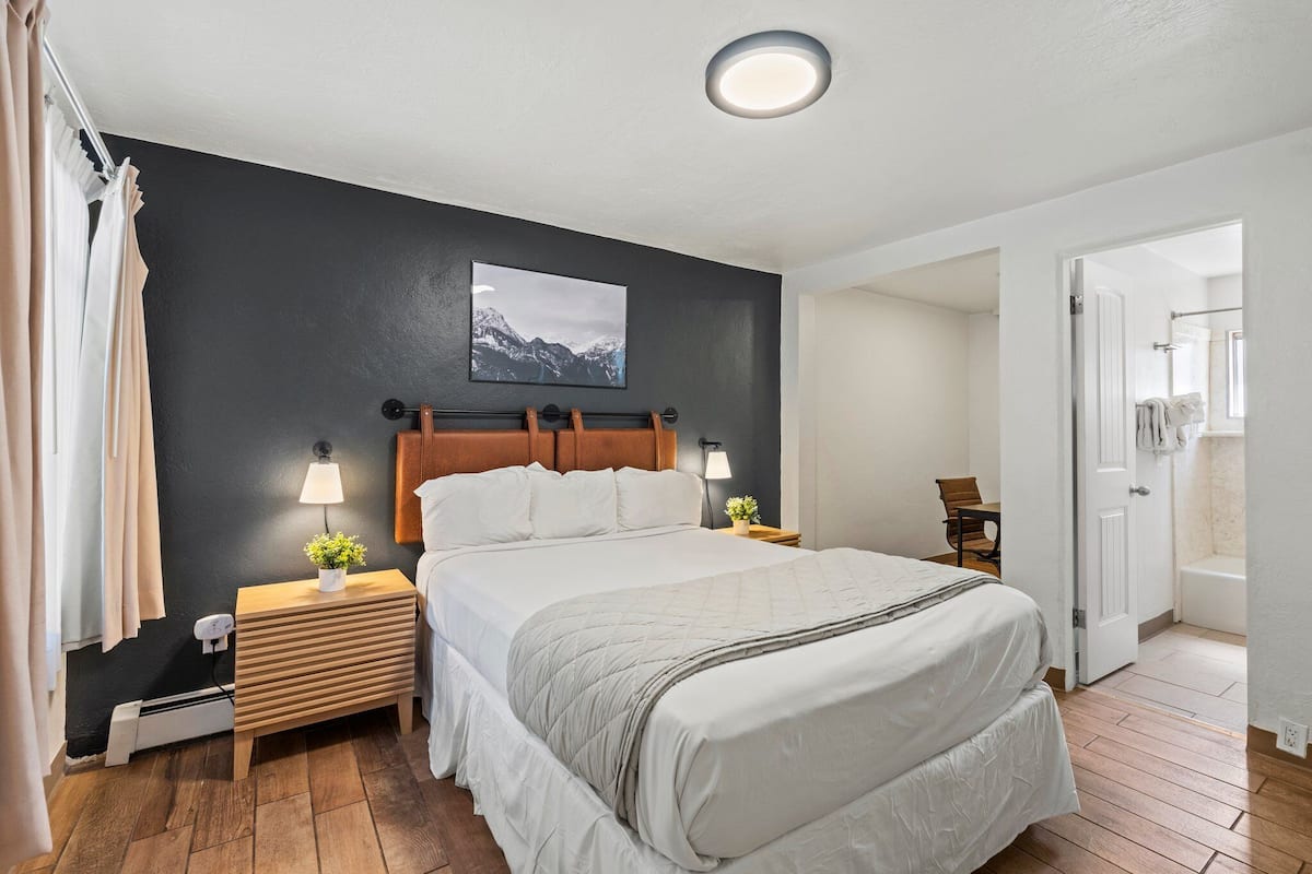 A bedroom with a large bed, bedside lamps, a nightstand with a plant, and a wall-mounted TV.