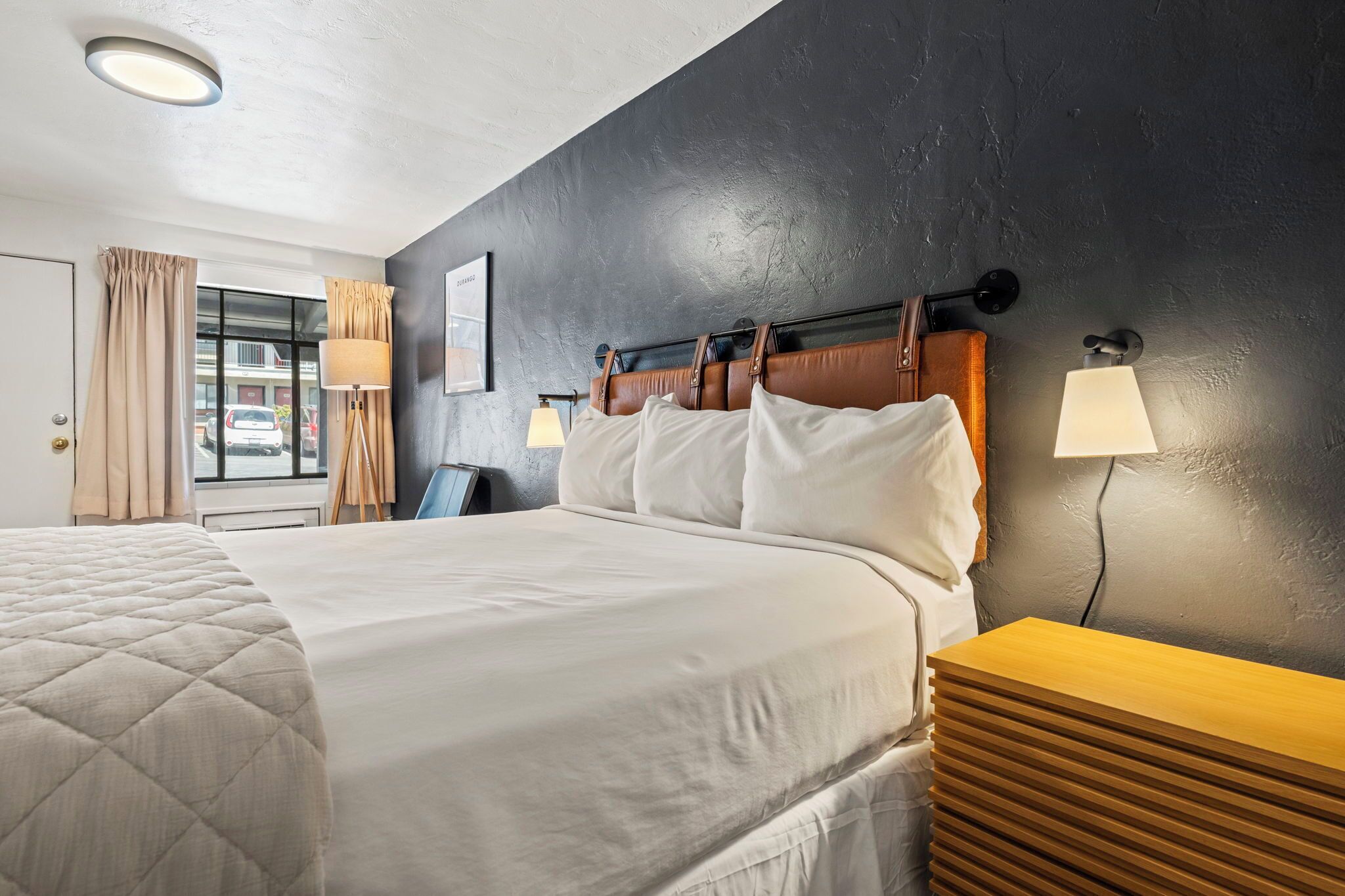 Une chambre d’hôtel avec un grand lit, une table de chevet en bois, un bureau et une fenêtre avec des rideaux.