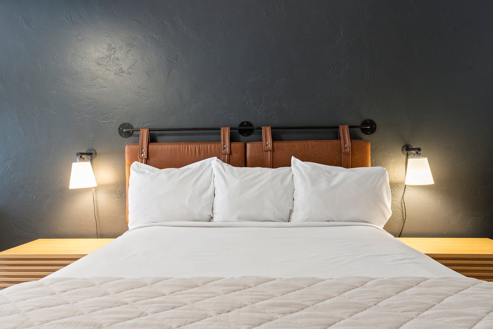 Ein Bett mit einem hölzernen Kopfteil, zwei Nachttischlampen und einer gesteppten weißen Decke.