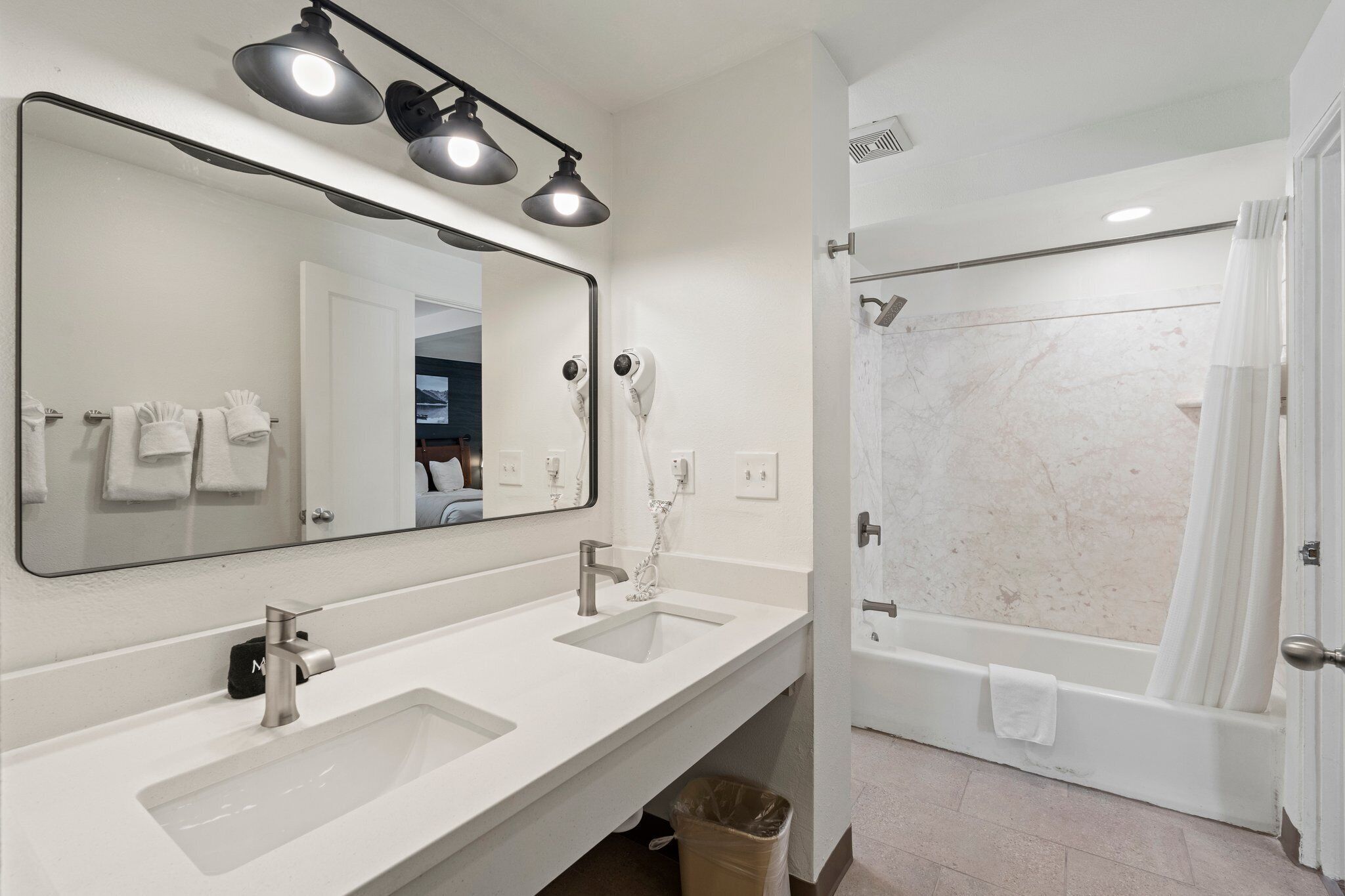 A modern bathroom with dual sinks, a large mirror, and a shower area.