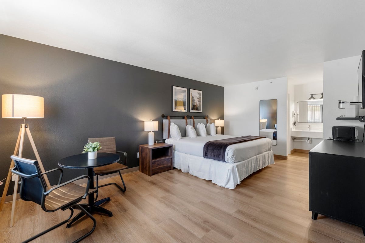 A modern hotel room with a bed, bedside tables, a desk, a chair, and a lamp.