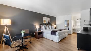 A modern hotel room with a bed, bedside tables, a desk, a chair, and a lamp.