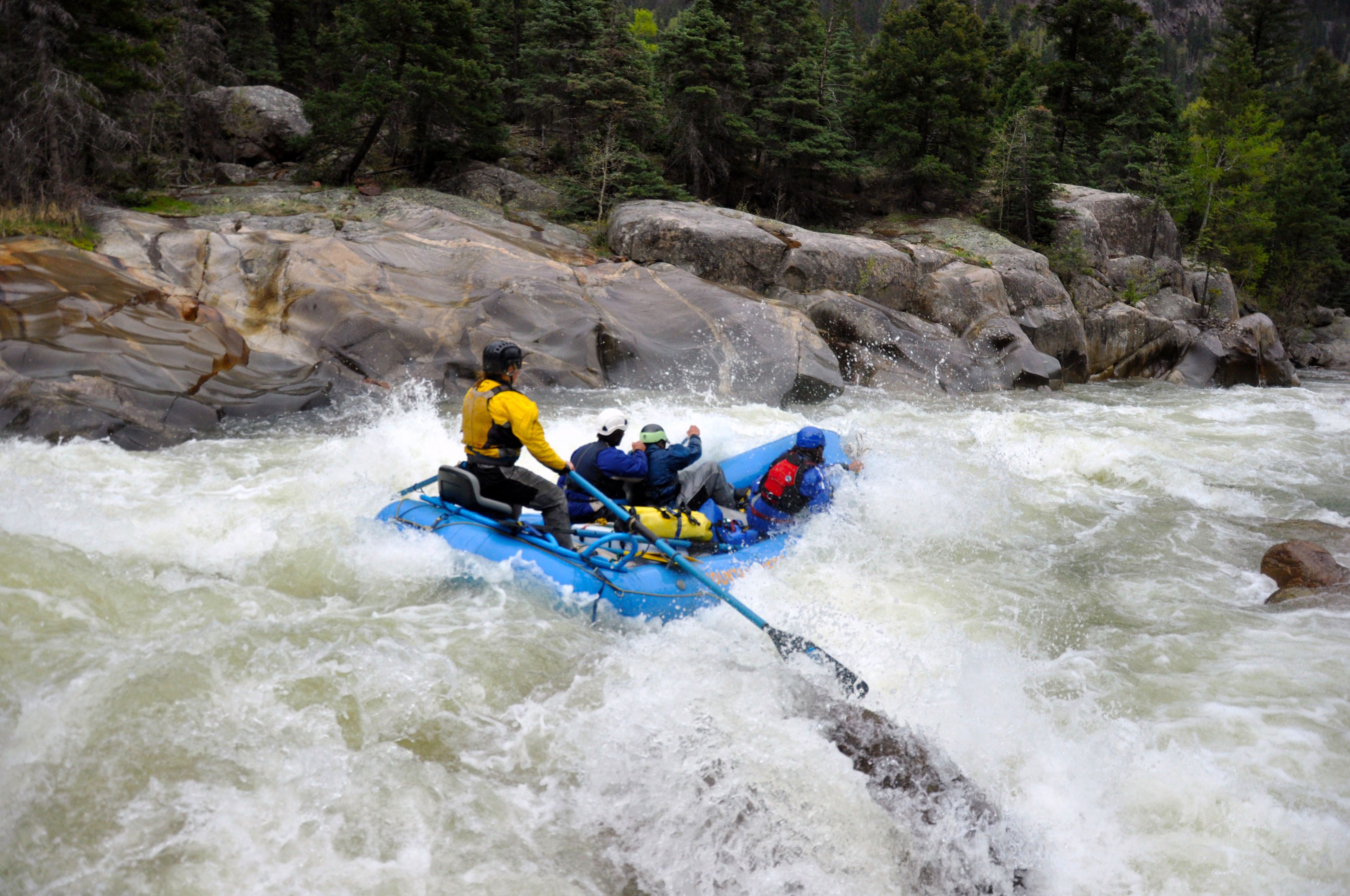 A group of people in a blue raft navigating through a river with white water rapids.
