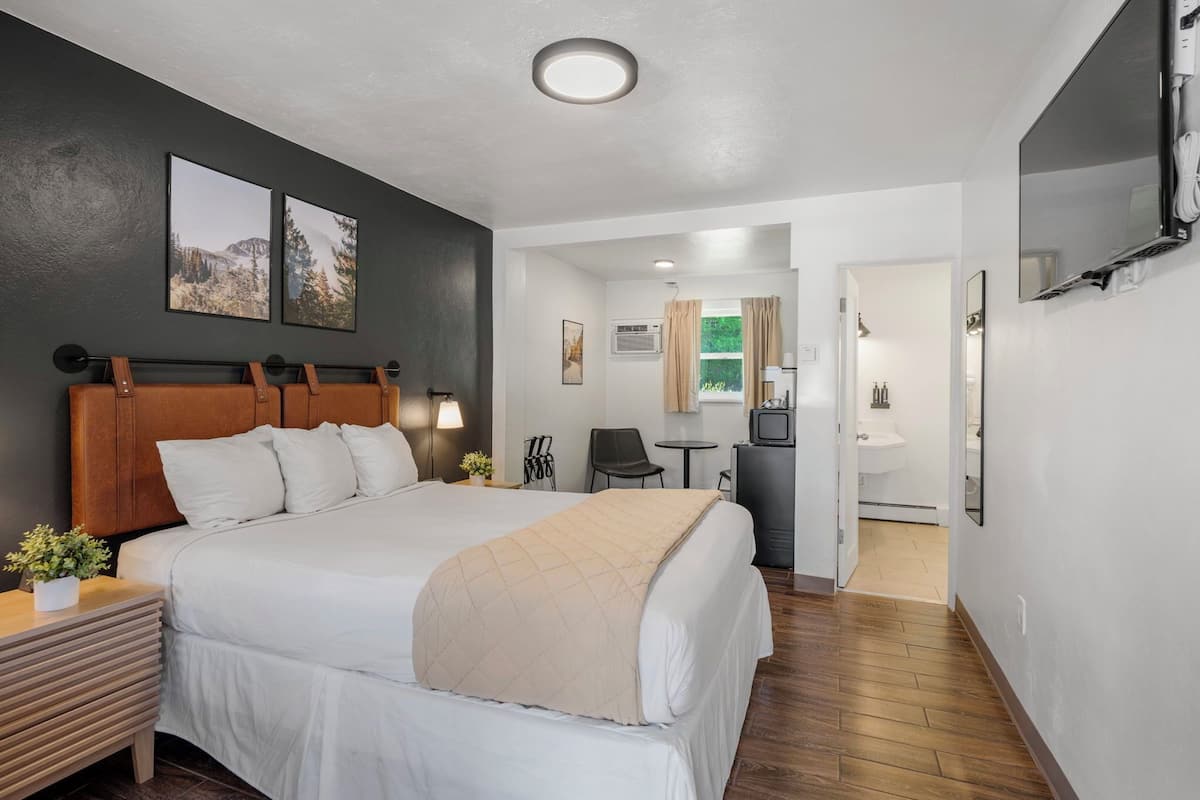 A hotel room with a large bed, a desk, a chair, a TV, and a bathroom visible through an open door.