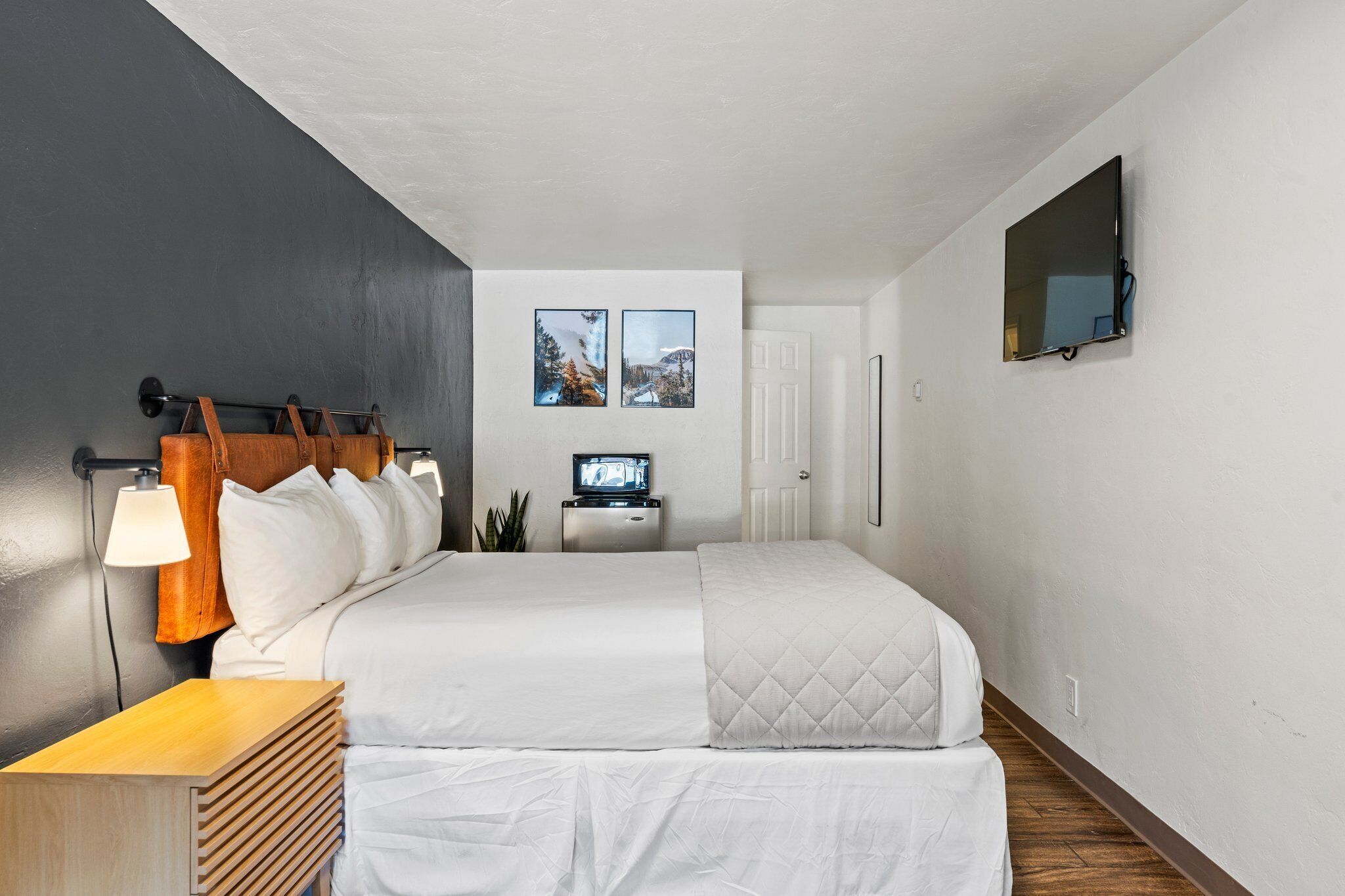 Et hotelværelse med seng, fjernsyn, skrivebord og fjernsyn ophængt på væggen.