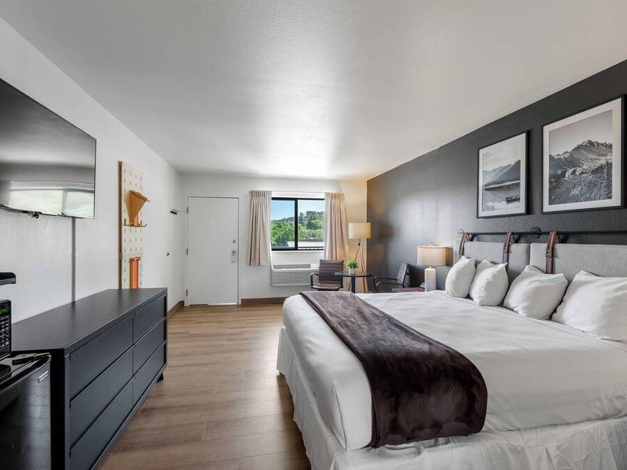 A modern hotel room with a large bed, a flat-screen TV, a desk with a lamp, and a window with curtains.