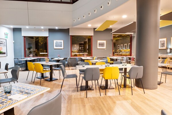 A modern dining area with multiple tables and chairs, large windows, and artwork on the walls. - Eurostars Amara (San Sebastián)