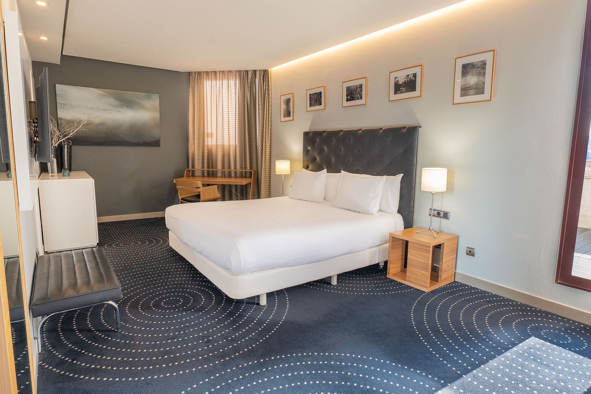 Et moderne hotelværelse med en stor seng, et skrivebord, en stol, en lampe og et billede på væggen.