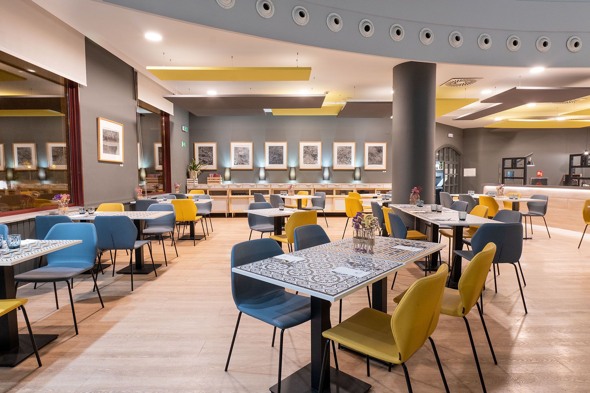 A modern dining area with multiple tables and chairs, a counter with a menu, and framed artwork on the walls.