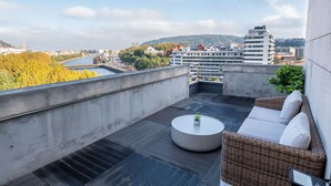 A rooftop terrace with a round table, wicker sofa, and a view of the cityscape. - Eurostars Amara (San Sebastián)