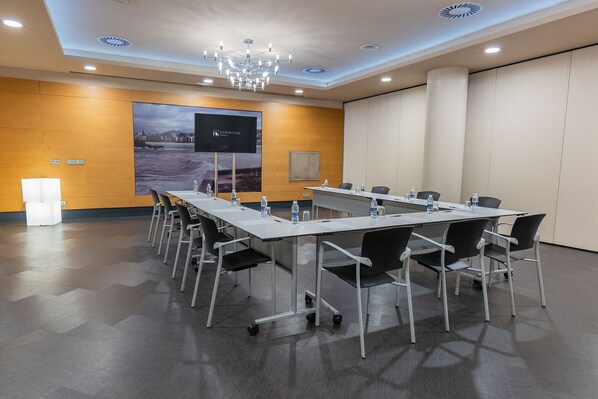 A conference room with a long table, chairs, a projector screen, and a chandelier. - Eurostars Amara (San Sebastián)