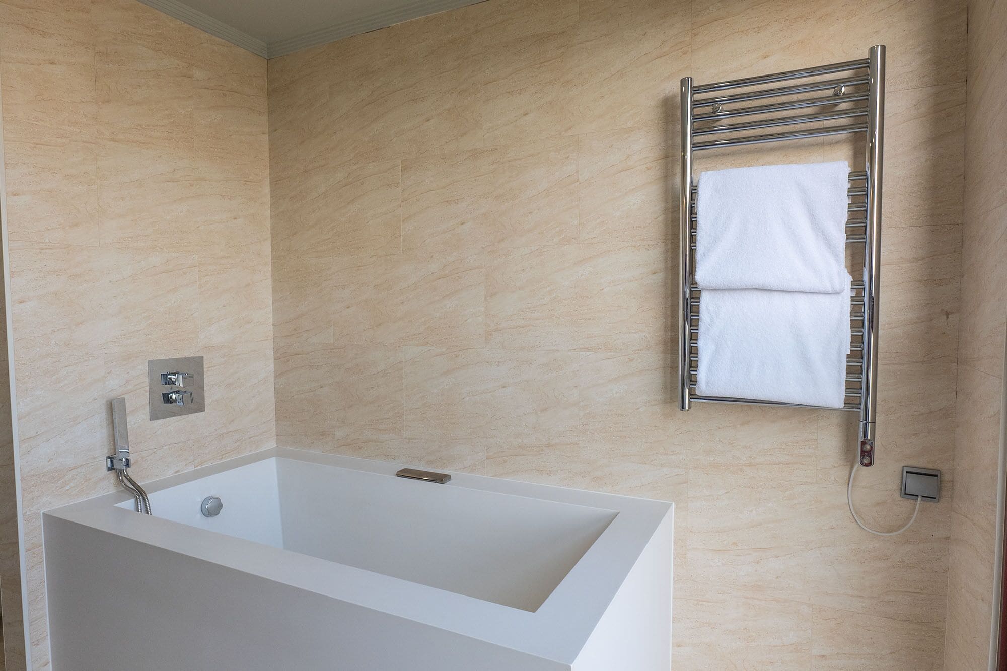 A modern bathroom with a rectangular bathtub, a towel rack with two towels, and a wall-mounted control panel.