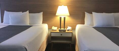 Ein Hotelzimmer mit zwei Betten, einem Nachttisch mit Lampe, einem gerahmten Bild an der Wand und einem hölzernen Kopfteil.