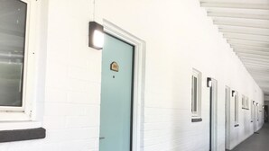 A corridor with doors numbered 201 to 205, white brick walls, and a window on the left. - San Diego Downtown Lodge (San Diego)