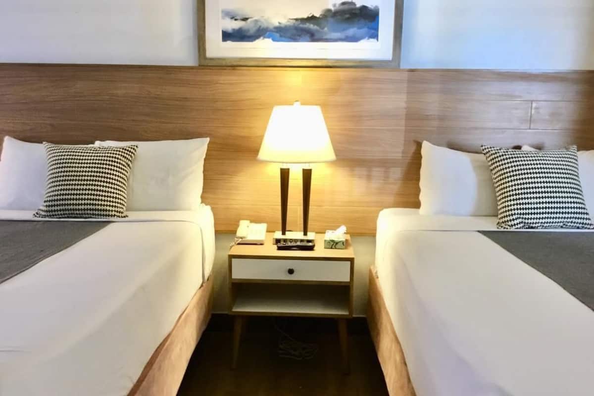 Une chambre d’hôtel avec deux lits, une table de chevet avec une lampe et un tableau encadré au mur.