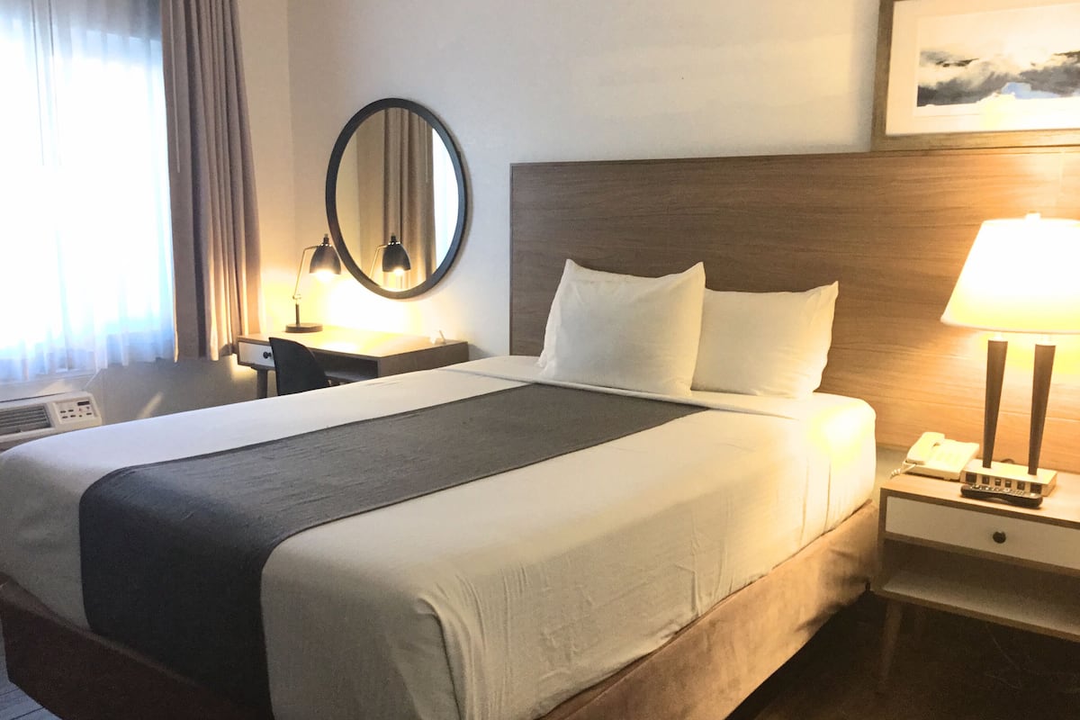 Une chambre d’hôtel avec un grand lit, une table de chevet avec une lampe, un miroir et un tableau au mur.