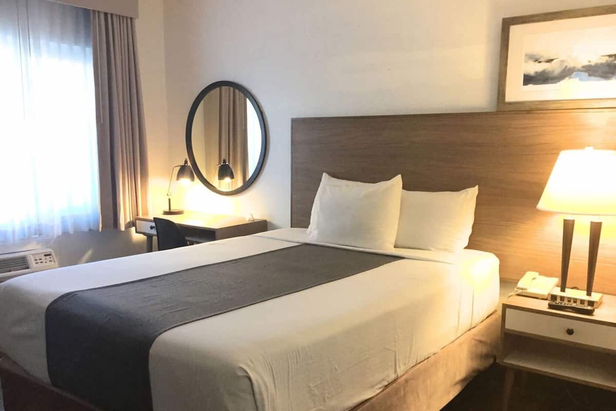 Une chambre d’hôtel avec un grand lit, des tables de chevet, un bureau, un miroir, une lampe et un tableau au mur.