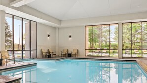 A swimming pool with clear water, surrounded by large windows offering views of trees and a lawn.