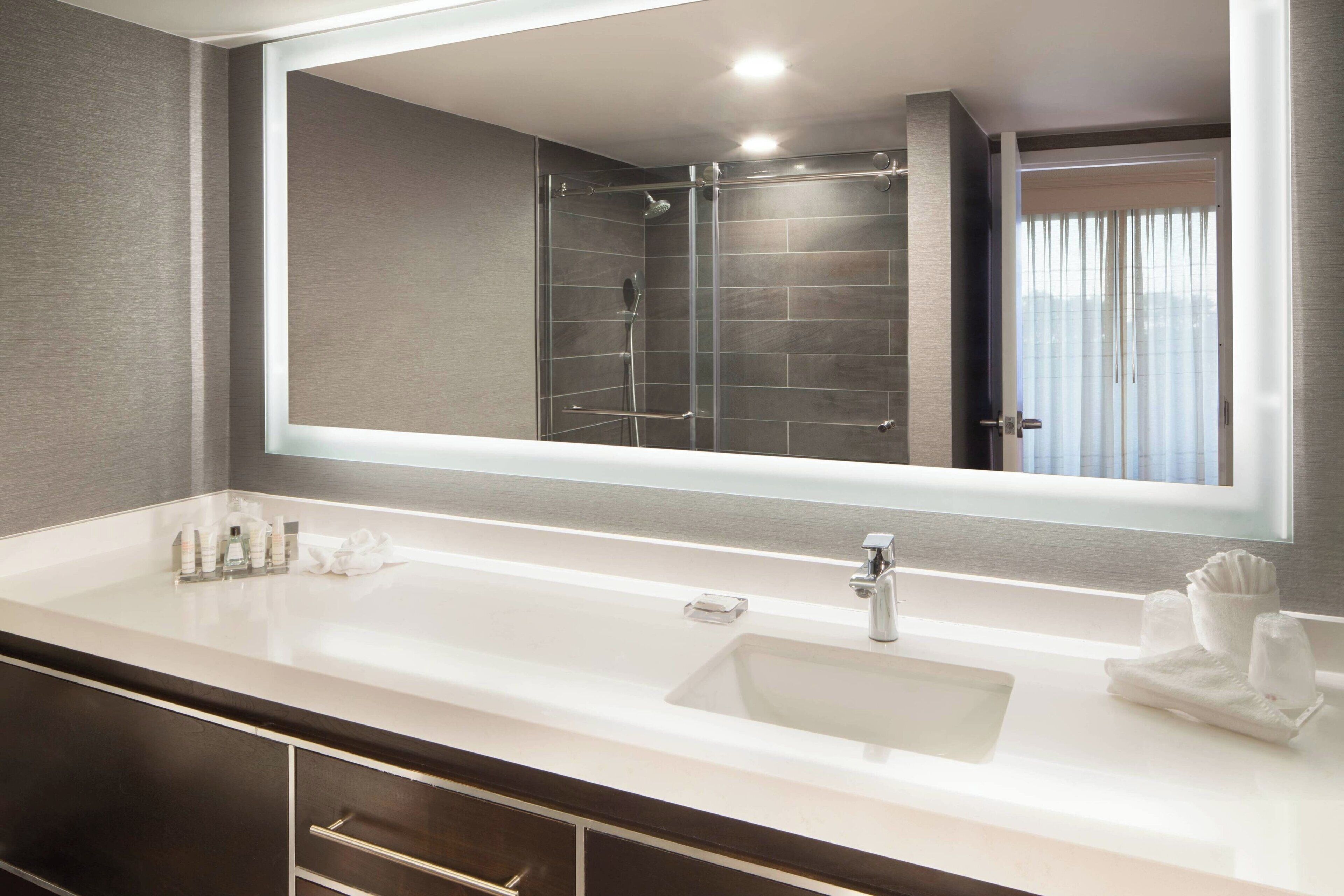 A modern bathroom with a large mirror, a white sink, and a shower area.