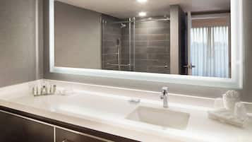 A modern bathroom with a large mirror, a white sink, and a shower area.