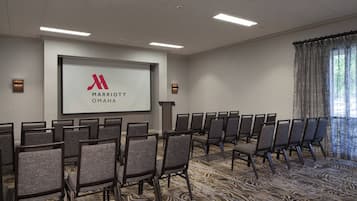 A conference room with rows of chairs, a large screen with 'Marriott Omaha' logo, and a carpeted floor.