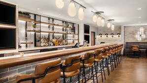 A modern bar area with a long counter, multiple shelves with glasses and bottles, and a row of bar stools.