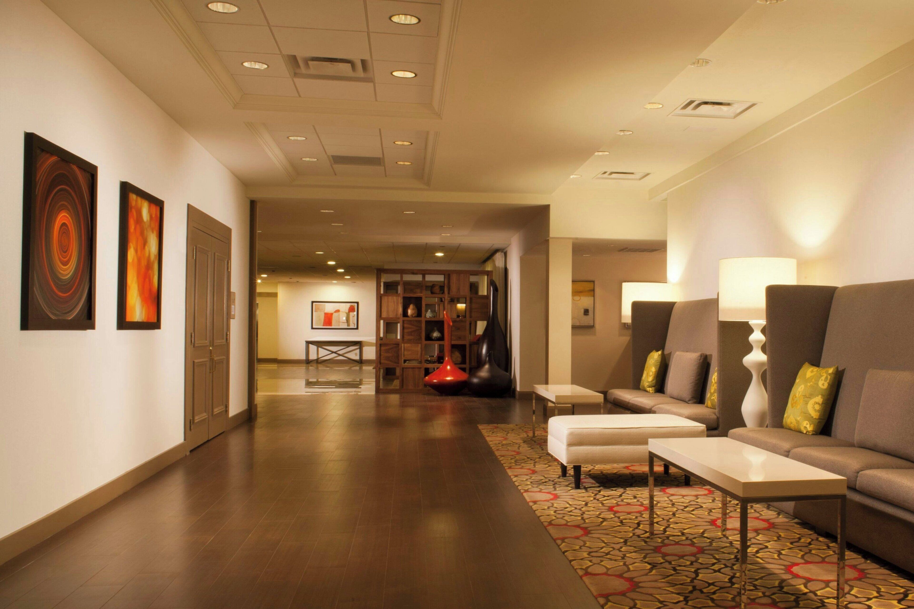 A hotel lobby with a long hallway, seating area with sofas and a coffee table, and a patterned carpet.