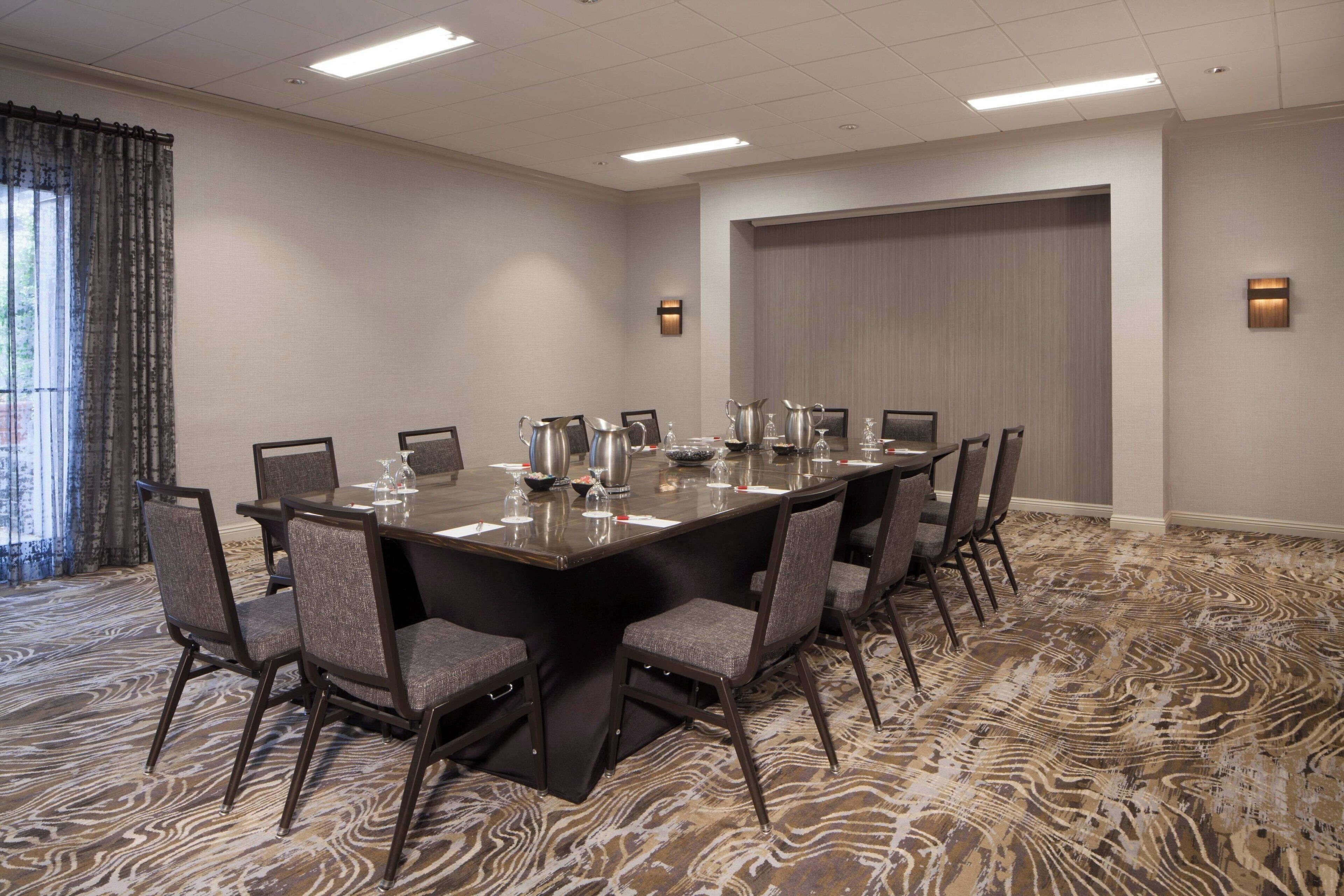 A conference room with a large rectangular table, multiple chairs, and a patterned carpet.